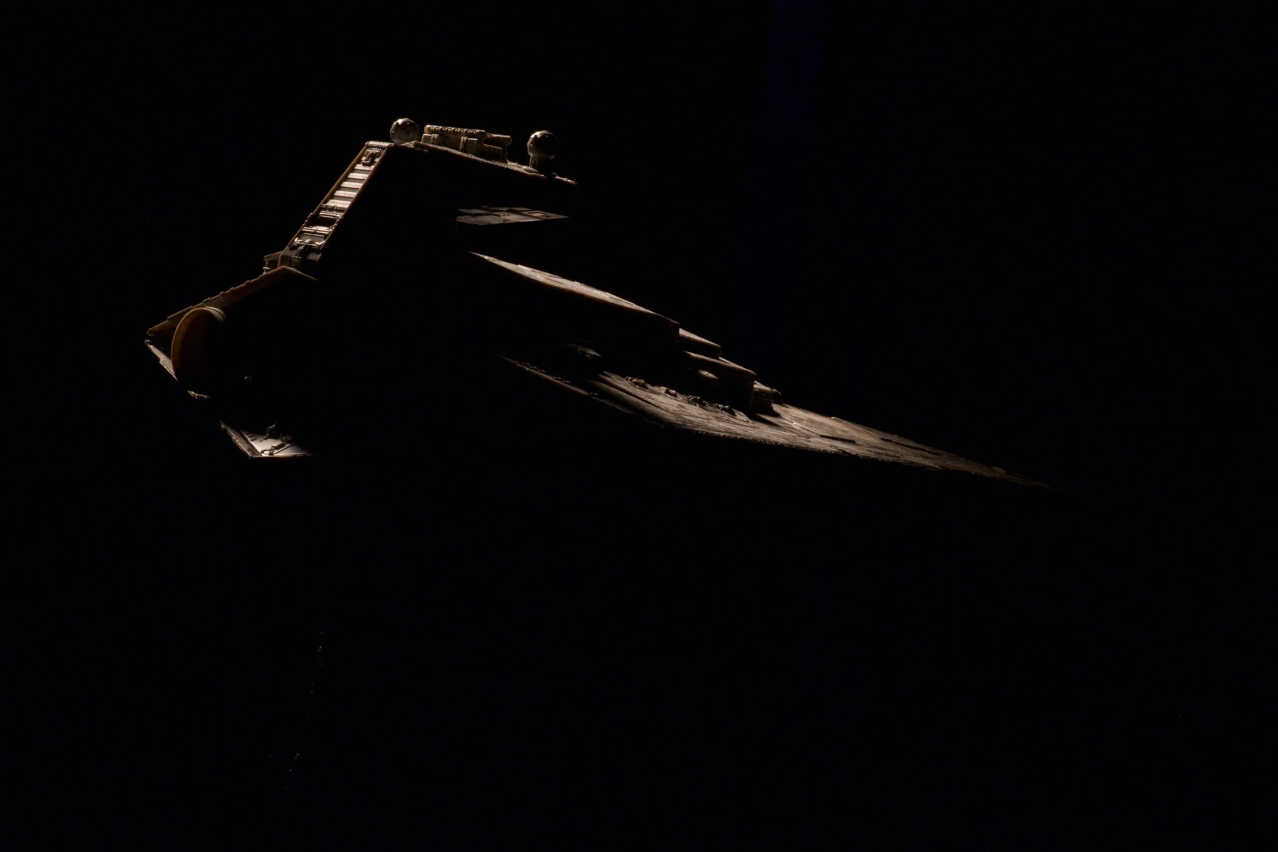 Miniature starship emerging from darkness under a single edge light