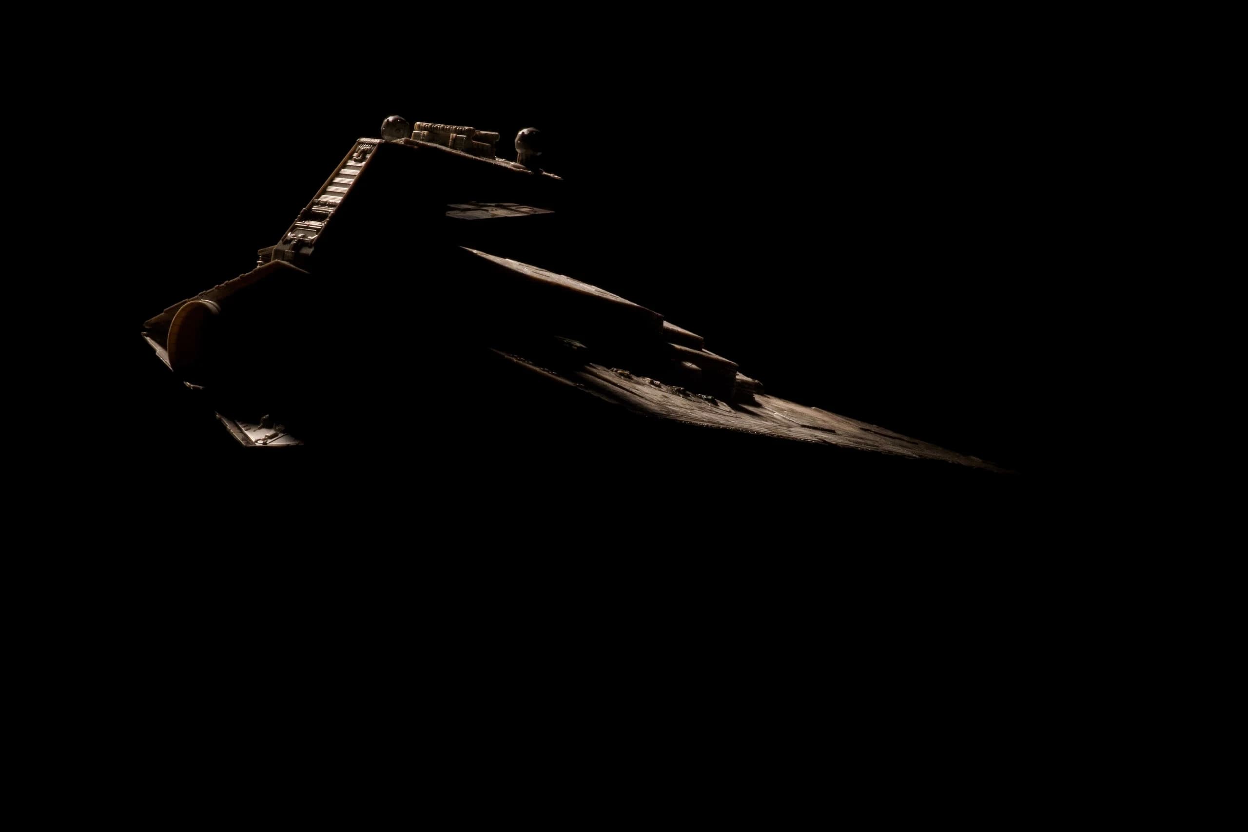 A physical starship miniature emerging from darkness under an edge light